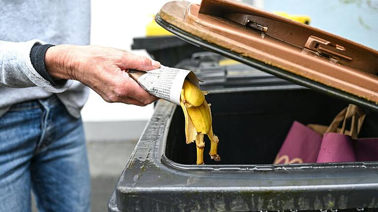 Eine Frau wirft in Zeitungspapier gewickelte Bananenschalen in eine Mülltonne für den Biomüll.&nbsp;