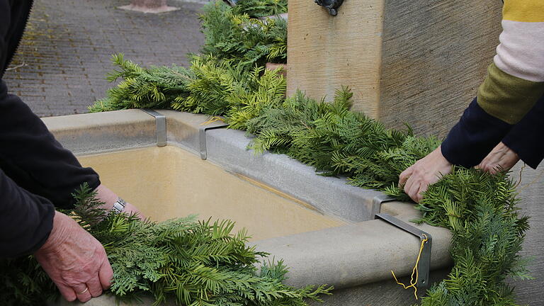 Die gebundenen Girlanden werden am Brunnen angebracht und mit Draht befestigt       -  Die gebundenen Girlanden werden am Brunnen angebracht und mit Draht befestigt