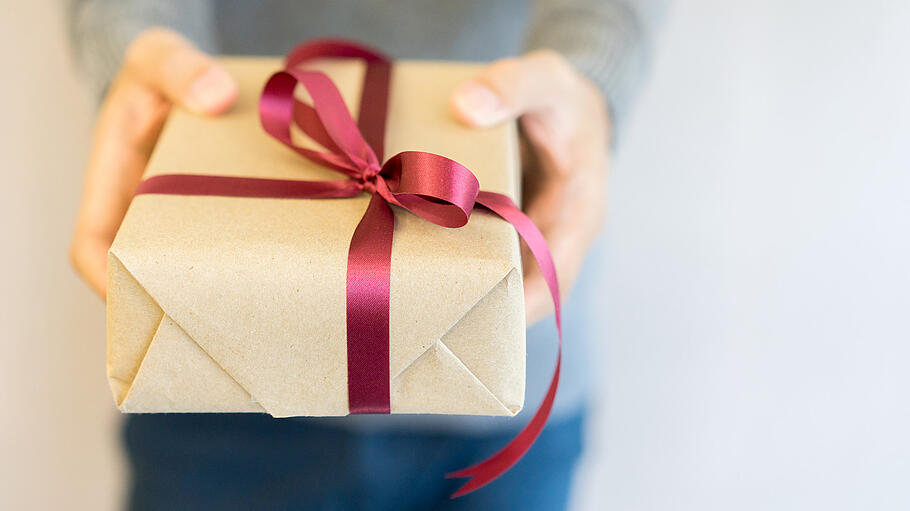 close up man wearing  sweater and hand holding tan box with red tied bow giving give to special person at living room for merry christmas and happy new year festival concept       -  close up man wearing  sweater and hand holding tan box with red tied bow giving give to special person at living room for merry christmas and happy new year festival concept