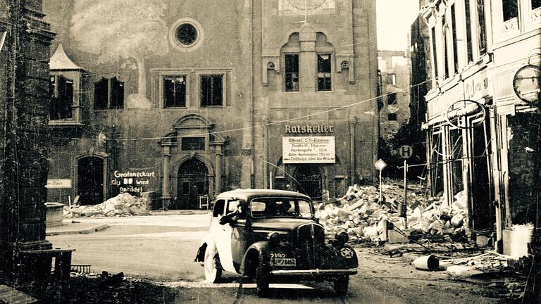 Oberbürgermeister Gustav Pinkenburg war dafür bekannt, dass er sich in seinem Auto durch die Straßen der zerstörten Stadt fahren ließ und über Lautsprecher Befehle erteilte. Das Foto entstand kurz nach der Einnahme Würzburgs; auf der Mauer des Grafeneckart steht noch eine Durchhalteparole.