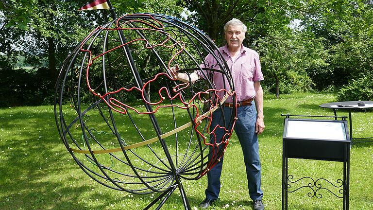 Die Hand am Äquator: Günther Hellmuth und sein aus Eisenstäben gefertigter Globus, der im Vordergrund Nord- und Südamerika in olympischem Rot zeigt.&nbsp;