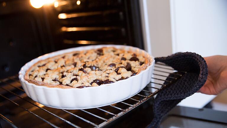 Eine Frau holt einen Pflaumenkuchen aus dem Ofen       -  Im Backofen sollte man den Kuchen eher im unteren Bereich backen, rät Backexpertin Annelie Ulrich.