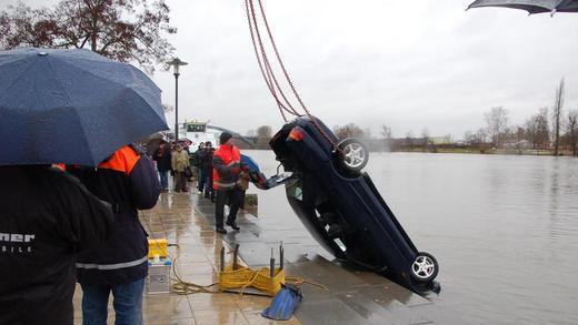 Auto landet im Main.       -  An Ketten befestigt wurde der Mitsubishi am Donnerstagmittag von Mitarbeitern des Wasser- und Schifffahrtsamtes mit einem Kran aus dem Main gehoben
