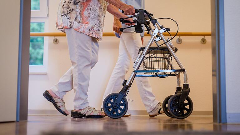 Eine Pflegekraft geht in einem Pflegeheim mit einer älteren Dame über einen Korridor.&nbsp;
