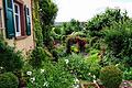 Harmonie von Haus und Garten: Gauben, Fensterläden und historische Baustoffe im Garten und an Nebengebäuden ergänzen sich mit Rosen, Clematis und Stauden.