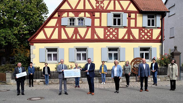 Vor dem Bürgerhaus überreichte Stiftungsrat Josef Schmid im Beisein der Akteure den Scheck an Iphofens Bürgermeister Dieter Lenzer. Stadtteilreferent Hans Brummer hält das Schild in Händen, das am Eingang des Gebäudes angebracht wird und an die Auszeichnung erinnert.