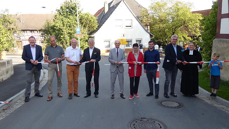 Nach nur viereinhalb Monaten konnte die Kreisstraße HAS46 wiedereröffnet werden. Im Bild von links: Alfons Schanz (Leiter der Tiefbauverwaltung), Michael Russ (Geschäftsführer Baufirma Rädlinger), Bürgermeister Markus Oppelt (Pfarrweisach), Landtagsabgeordneter Steffen Vogel, Landrat Wilhelm Schneider, Erika Stubenrauch (Ingenieurbüro Stubenrauch), Jan-Michael Derra (Ingenieurbüro Stubenrauch), Bürgermeister Helmut Dietz (Untermerzbach), Pfarrerin Sonja von Aschen und ein junger Dorfbewohner, der sich auch über die neue Straße freut.