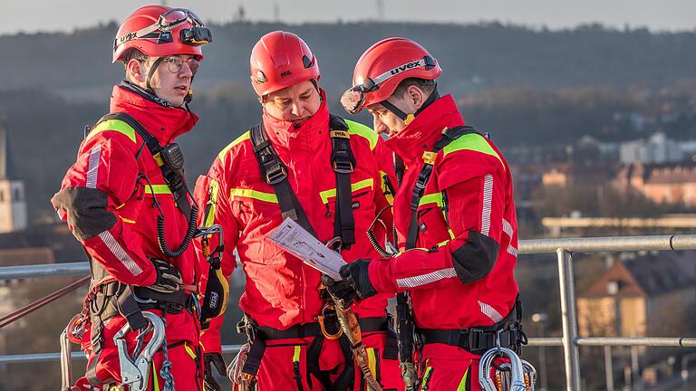 Über Würzburg beraten sich die Höhenretter über das Übungsszenario. Neben dem Auffanggurt tragen die Feuerwehrmänner etliche Karbinerhaken, Seile und Helme an ihrer Ausrüstung. Über Würzburg beraten sich die Höhenretter über das Übungsszenario. Neben dem Auffanggurt tragen die Feuerwehrmänner etliche Karbinerhaken, Seile und Helme an ihrer Ausrüstung.