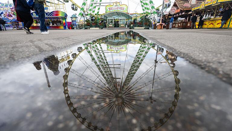 Stuttgarter Frühlingsfest 2024.jpeg       -  Ein Riesenrad spiegelt sich in einer Pfütze auf dem Festgelände des Stuttgarter Frühlingsfestes.