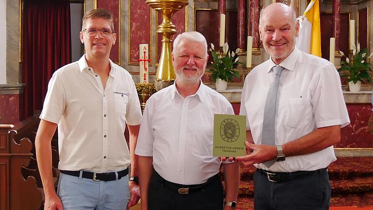 Schriftführer und Ortsobmann Jürgen Wolf (links) und Vorstand Eberhard Nuß (rechts) vom Katholischen Männerverein St. Hubertus, Fährbrück, begrüßen Augustinerpater Matthäus Klein als ihren neuen Präses und überreichen ihm eine druckfrische neue Satzung mit Rückblicken und Infos zu den einzelnen Ortsgruppen.