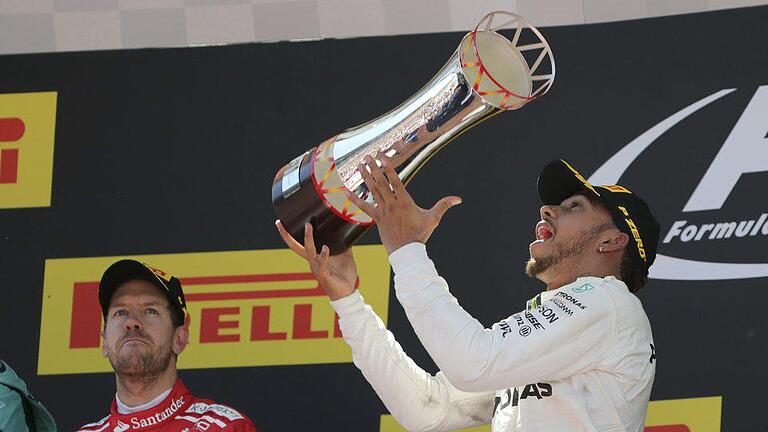 Erster und Zweiter       -  Lewis Hamilton jubelt über seinen Sieg, Sebastian Vettel (l) applaudiert mit ernster Miene. Foto: Emilio Morenatti