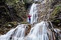 Eine Frau steht bei regnerischem Wetter am Wasserfall und nimmt ein Foto mit ihrem Smartphone auf.jpeg       -  Für Erlebnisse in freier Wildbahn gibt es spezielle Outdoor-Smartphones.