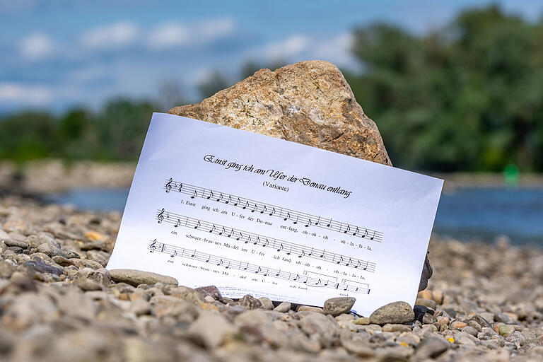 Ein Notenblatt mit dem Liedtext 'Einst ging ich am Ufer der Donau entlang' wird am Donauufer gehalten. In dem Lied wird die Vergewaltigung eines schlafenden Mädchens beschrieben.&nbsp;
