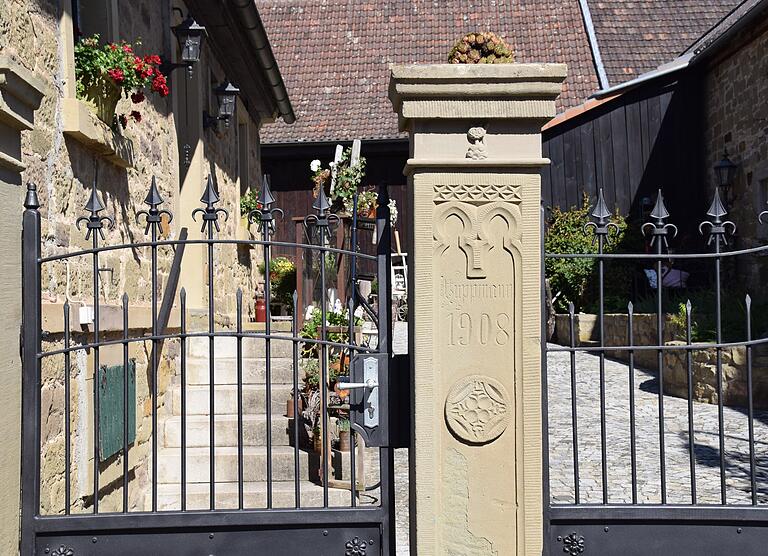 Am sandsteinernen Torpfosten von 1908 ist das ganz neue kunstgeschmiedete Eisentor im alten Stil befestigt.