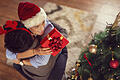 Couple exchanging Christmas presents       -  High angle view of a beautiful couple in love, wearing Santa hats, standing next to a nicely decorated Christmas tree, exchanging Christmas presents and hugging