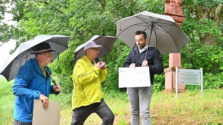 Pilgerführer Peter Neubert und Wallfahrervereinsvorsitzender Gerhard Lang (von links) überreichten Großrinderfelds Bürgermeister Johannes Leibold bei strömendem Regen einen Scheck über 500 Euro, der einen Anteil an den Restaurierungskosten des Bildstocks von 1650 decken soll.