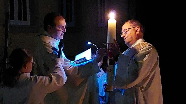 Der wichtigste Gottesdienst des Jahres: die Feier der Osternacht, die Mutter aller Nachtwachen. Pfarrer Reder (links) beginnt den ersten Teil dieser uralten Liturgie andächtig und würdevoll mit der Lichtfeier, wie hier auf dem Foto aus dem Jahr 2023 im Heidenfelder Pfarrgarten. Die Osterkerze hält Diakon Albert Hein (rechts) in den Händen. Der wichtigste Gottesdienst des Jahres: die Feier der Osternacht, die Mutter aller Nachtwachen. Pfarrer Reder (links) beginnt den ersten Teil dieser uralten Liturgie andächtig und würdevoll mit der Lichtfeier, wie hier auf dem Foto aus dem Jahr 2023 im Heidenfelder Pfarrgarten. Die Osterkerze hält Diakon Albert Hein (rechts) in den Händen.