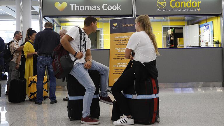 Zwei Passagiere warten sitzend auf ihren Koffern neben dem Büro von Condor und Thomas Cook im Flughafen Palma de Mallorca.