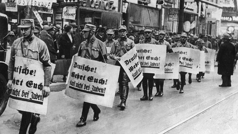 Männer der SA bei einem Hetzmarsch durch die Straßen von Berlin gegen die jüdische Bevölkerung Deutschlands, Aufnahme von 1938. Die mitgeführten Plakate tragen die Aufschrift 'Deutsche wehrt Euch! Kauft nicht bei den Juden!'.