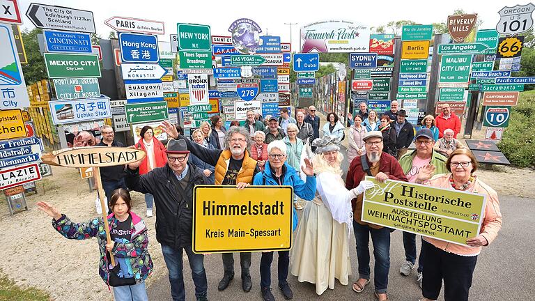 Bei der Schilderübergabe von links: Herbert Hemmelmann, Klaus Beer, Marie-Luise Schäfer, 'Christkindl' Heidrun Koch, Willfried Stamm und ganz rechts Rosemarie Schotte. Im Hintergrund sind Ehrenamtliche der Himmelstädter 'Christkindl-Postfiliale' zu sehen.