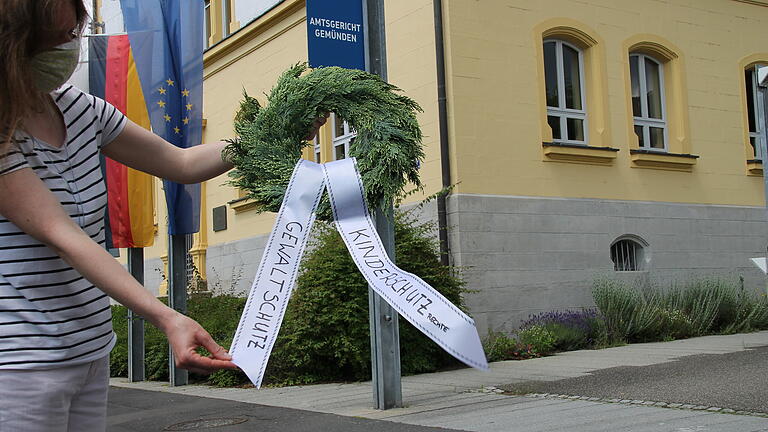 Verena M. legt vor dem Amtsgericht Gemünden einen Kranz nieder und trägt damit Gewaltschutz und Kinderschutz symbolisch zu Grabe.