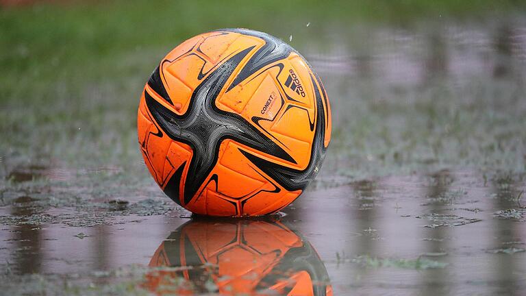 Ein Ball liegt auf einem Sportplatz in einer Pfütze. Durch teils ergiebige Niederschläge an den vergangenen Tagen sind zahlreiche Fußballplätze in der Region unbespielbar.