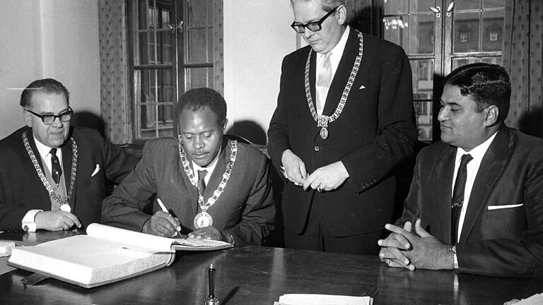 Partnerstadt       -  26. Januar 1967: Der OB von Mwanza, Halfani Hassani, trägt sich ins Goldene Buch der Stadt Würzburg ein. Gesellschaft leisten ihm Bürgermeister Joseph Seitz (links), OB Helmuth Zimmerer (stehend) und Mwanzas Oberstadtdirektor Sachak.