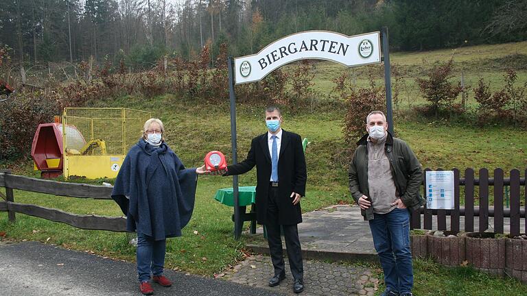 Ein Defibrillator für Emmerichsthal: Marco Löffler von der Raiffeisenbank Main-Spessart (Mitte) überreicht das neue Gerät an Lioba Zieres und Mitinitiator Thorsten Becker (rechts).