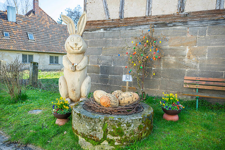 In Ruppach hat Künstler Bernd Schmidt einen Osterbrunnen gestaltet. Hier lacht ein großer geschnitzter Hase die Besucherinnen und Besucher an.