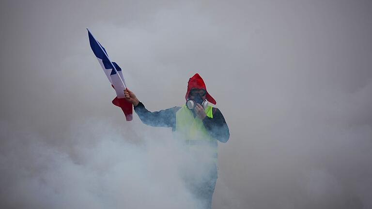 Ein Demonstrant in Paris inmitten einer Tränengaswolke. Menschen in neongelben Warnwesten und teilweise vermummt haben sich Straßenkämpfe mit den Sicherheitskräften geliefert.