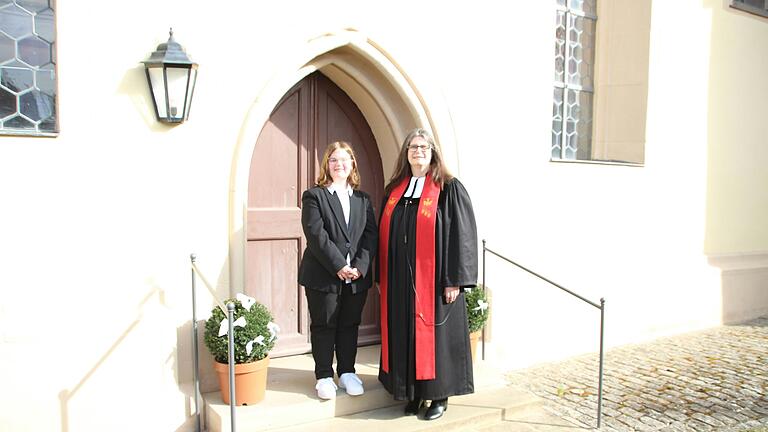 Konfirmandin Lea Barthelmes mit Pfarrerin Beate Hofmann-Landgraf vor der St. Jakobuskirche in Irmelshausen.