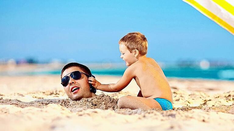 happy kid helping father in sand talk on mobile phone       -  Wer einen Urlaub im EU-Ausland plant, kann sich freuen: Handy-Telefonate, SMS-Versand und das Surfen im Internet kosten bald nicht mehr als zuhause.
