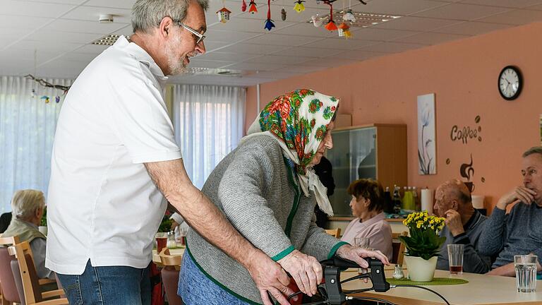 Pflegehelfer Michael Schraud unterstützt die aus der Ukraine stammende Seniorin beim Gang durch die Tagespflege.