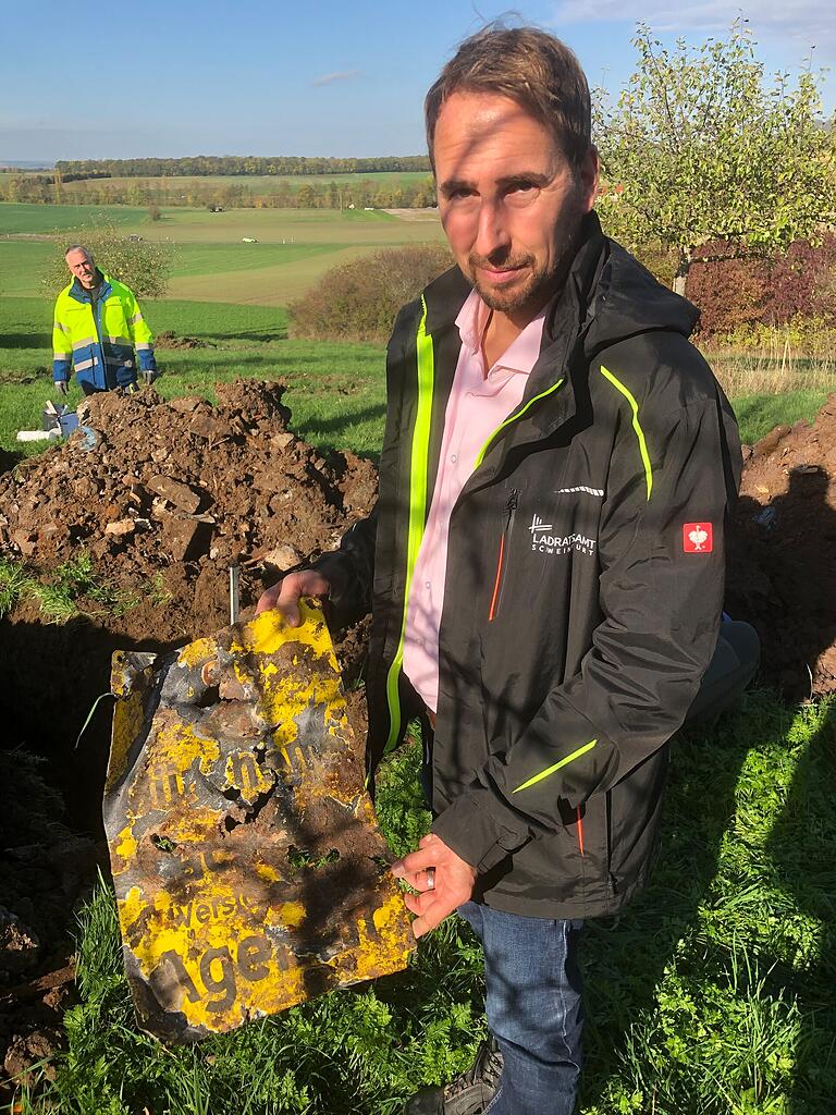 Oliver Seufert zeigt das gelbe Werbeschild einer Versicherungsagentur.