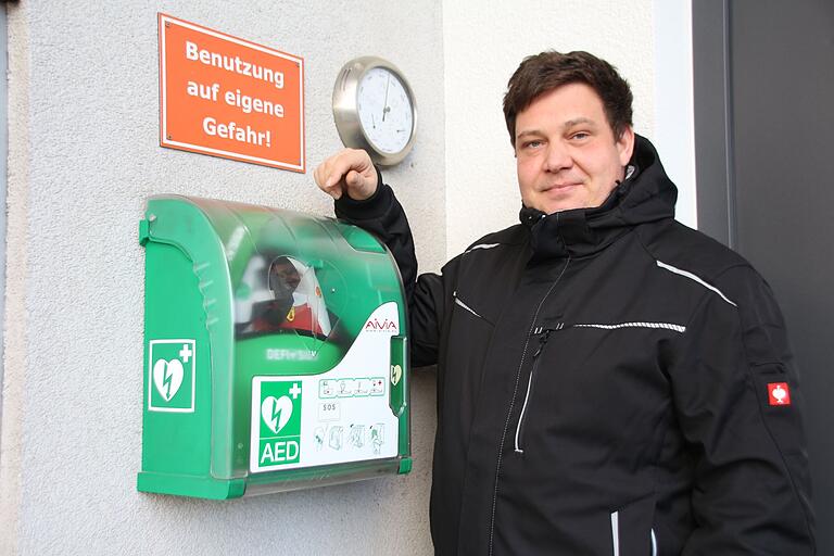 Adrian Treutlein steht neben dem Defibrillator, der in Gernach neben einer Autowerkstatt hängt. Damit hat er mit drei weiteren Helfern einem Mann mit Herzkammerflimmern das Leben gerettet hat.