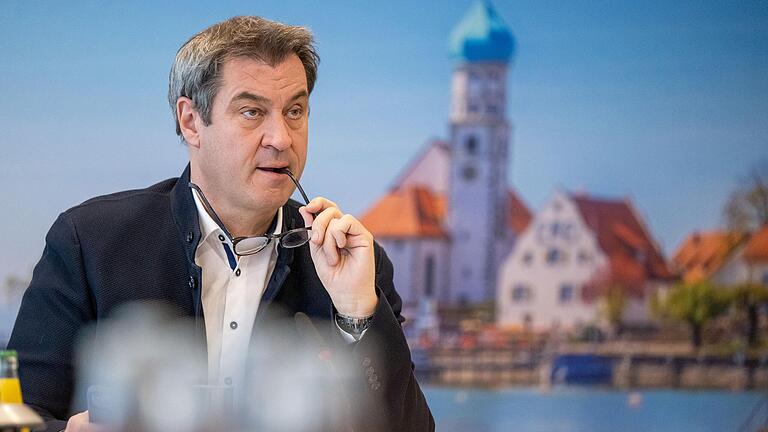 Markus Söder (CSU), Ministerpräsident von Bayern, sitzt vor Beginn einer Online-Sitzung des bayerischen Kabinetts an seinen Platz vor einer Fotowand. (Archivbild)