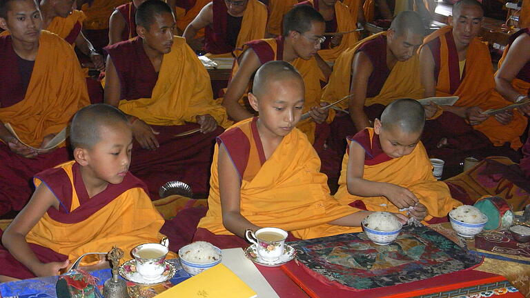 Mönche und Jungen, die als Wiedergeburten von Lamas erkannt wurden, bei der Puja. Die Besucher der oft länger dauernden Zeremonie werden meist gut versorgt, hier mit Tee und süßem Reis.