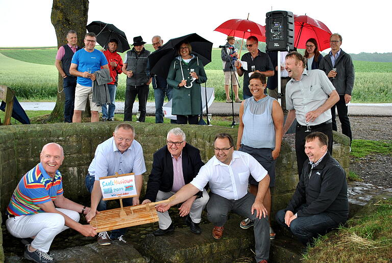 Die Saalequelle lieferte nur wenig Wasser, um das Floß hineinzusetzen, mit dabei sind (von links) Landrat Thomas Habermann, Landrat Thomas Bold, Dr. Klaus Reder, Bürgermeister Michael Custodis, Projektleiter Kuno Holzheimer und (dahinter, stehend) Bürgermeisterin Angelika Götz neben Kreisheimatpfleger Reinhold Albert.