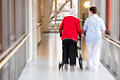Bericht spricht von Kipppunkt in der Pflege in Bayern.jpg       -  Eine Pflegerin geht mit einer Bewohnerin des Pflegeheims und einem Rollator über den Flur.