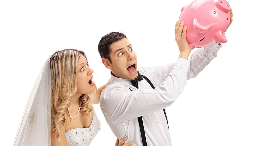 Shocked newlywed couple shaking an empty piggybank       -  Shocked newlywed couple shaking an empty piggybank isolated on white background