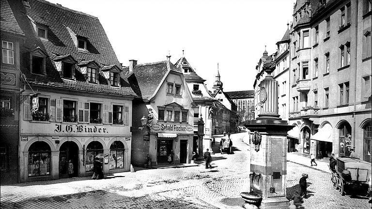 Blick in die Zeller Straße mit der Deutschhauskirche und dem Dreikronenbrunnen. Die beiden Gebäude in der Bildmitte mit den prächtigen Hausmadonnen stehen noch, vom Haus links sind nur drei Bögen erhalten. Die Häuser der rechten Straßenseite fielen den Bomben des 16. März 1945 zum Opfer.