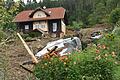 Nach Unwettern in Österreich.jpeg       -  Nach einem neuen Erdrutsch am Wochenende in Kärnten liegt dieses Auto unweit eines Hauses auf dem Dach, während im Hintergrund Aufräumarbeiten mit einem Bagger stattfinden.