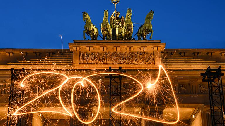 Die Zahl 2021 ist mit einer Wunderkerze während einer Langzeitbelichtung vor dem Brandenburger Tor in den Abendhimmel geschrieben. Was mag das neue Jahr nach dem Seuchenjahr 2020 bringen?