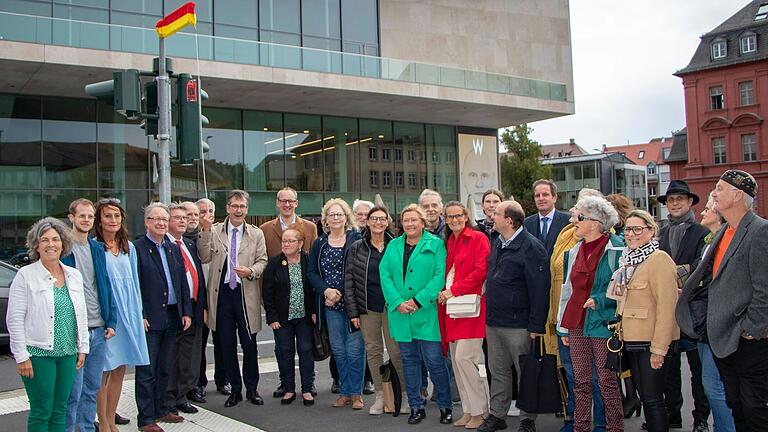 Oberbürgermeister Christian Schuchardt hat sichtlich Freude an der Enthüllung des neuen Straßennamensschilds 'Theaterplatz'. Zahlreiche Mitglieder des Stadtrats, Baureferent Benjamin Schneider, Kulturreferent Benedikt Stegmayer, Altbürgermeisterin Marion Schäfer-Blake, Altbürgermeister Dr. Adolf Bauer, der Intendant des Mainfranken Theaters Würzburg, Markus Trabusch, Stadtheimatpfleger Dr. Hans Steidle, Landtagsmitglied Kerstin Celina und Anwohnerinnen und Anwohner des Theaterplatzes nahmen an der Enthüllung teil.