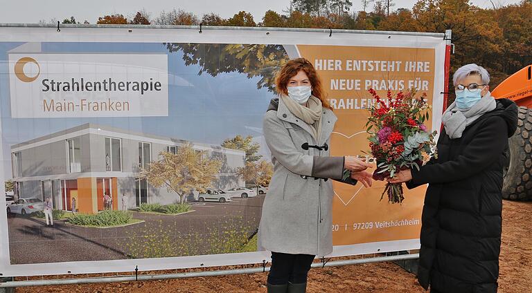 Ihre Freude über die Ansiedlung der Praxis für Strahlentherapie Mainfranken als erster Bauabschnitt ihres Gesundheitszentrums bringt Andrea Mehlig (rechts) mit einem Blumenstrauß zum Ausdruck, den sie Dr. Sandra Röddiger, der Geschäftsführerin der Radio-Onkologie-Netzwerk GmbH (RON) mit Sitz in Aalen überreicht.