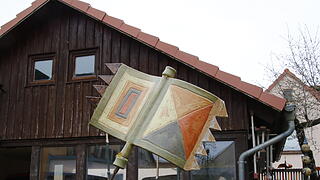 Eine Keramikflagge aus Erdtönen steht vor einer kleinen Scheune im Garten.       -  Eine Keramikflagge aus Erdtönen steht vor einer kleinen Scheune im Garten.