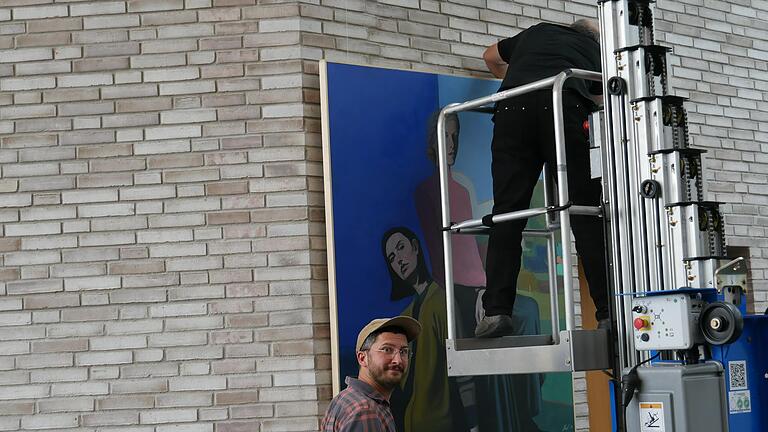 Der Künstler Jaroslav Drazil vor einem seiner Werke, das mit einem Hubsteiger im Foyer an einer hohen Wand der Stadthalle von einem Techniker aufgehängt wird Der Künstler Jaroslav Drazil vor einem seiner Werke, das mit einem Hubsteiger im Foyer an einer hohen Wand der Stadthalle von einem Techniker aufgehängt wird