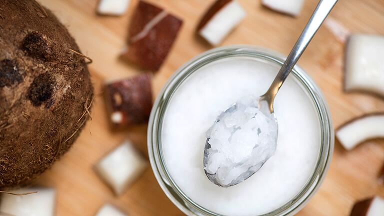 Festes Kokosöl auf einem Löffel       -  Echtes natives Kokosöl verleiht Gerichten einen aromatischen Geschmack, sollte jedoch wegen seiner gesättigten Fettsäuren nur sparsam verwendet werden.