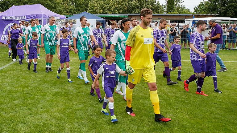 Die Traditionsmannschaft von Werder Bremen (vorne) und die Auswahl des TSV Grombühl laufen zum Freundschaftsspiel im Rahmen des Vereinsjubiläums auf dem Sportplatz ein.