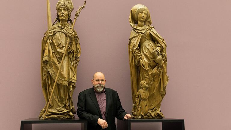 Wolfgang Schneider, Kurator der Sonderausstellung „Riemenschneider X Stoss' im Museum am Dom in Würzburg, zwischen dem heiligen Kilian und der heiligen Elisabeth, zwei Riemenschneider-Figuren des Münnerstädter Magdalenenaltars.&nbsp;